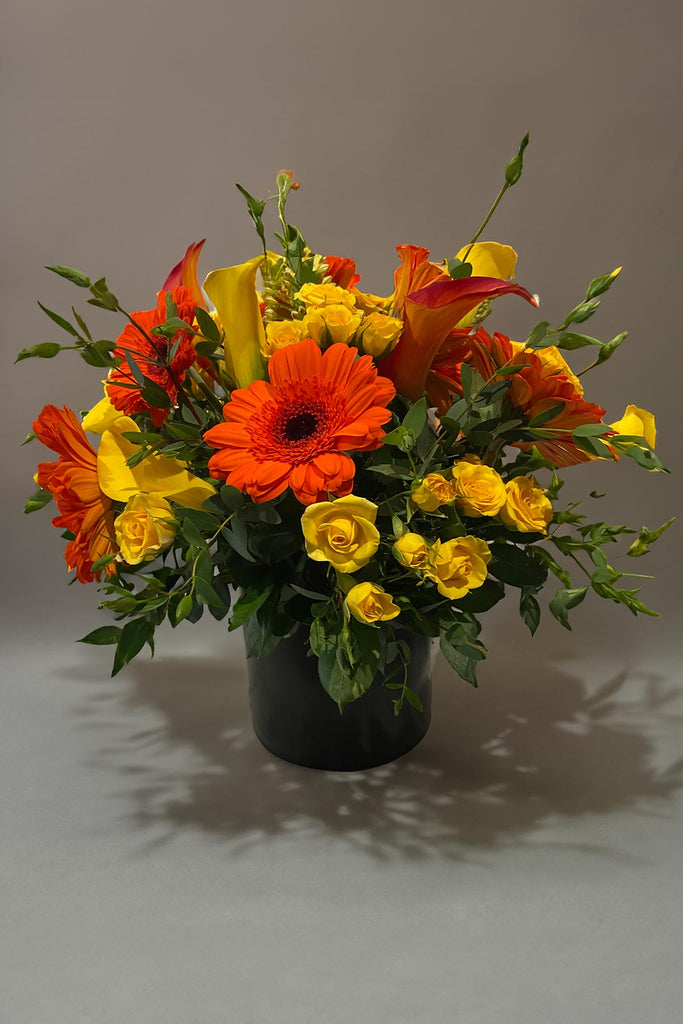 Orange and yellow flower arrangement in a black vase with roses, gerbera daisies and calla lilies