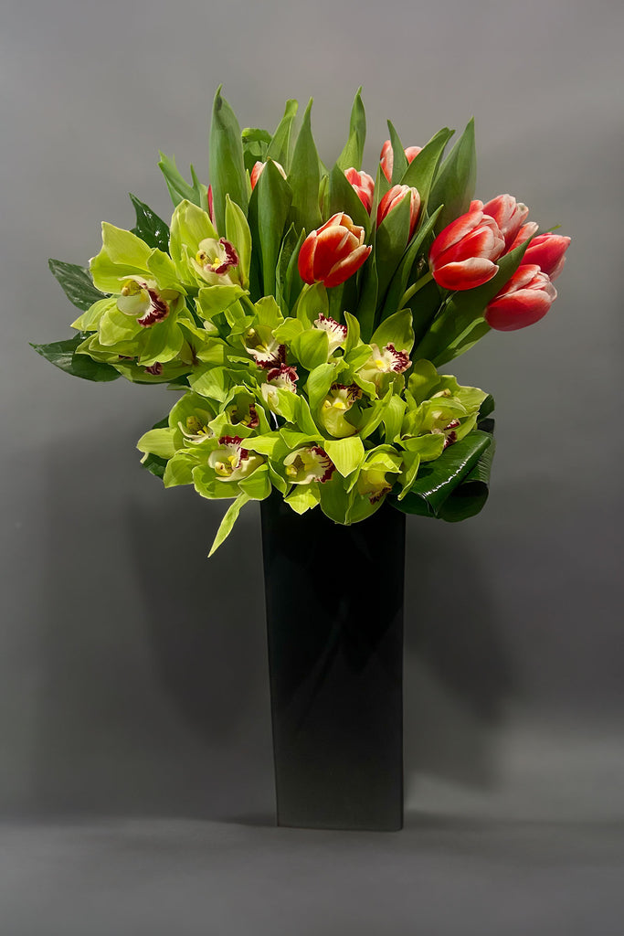 Tall flower arrangement with green orchids and tulips in a black vase