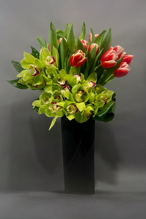 Tall flower arrangement with green orchids and tulips in a black vase