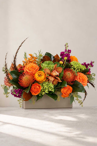 Autumn floral arrangement with orange roses, textured seasonal blooms, and greenery in a modern rectangular container