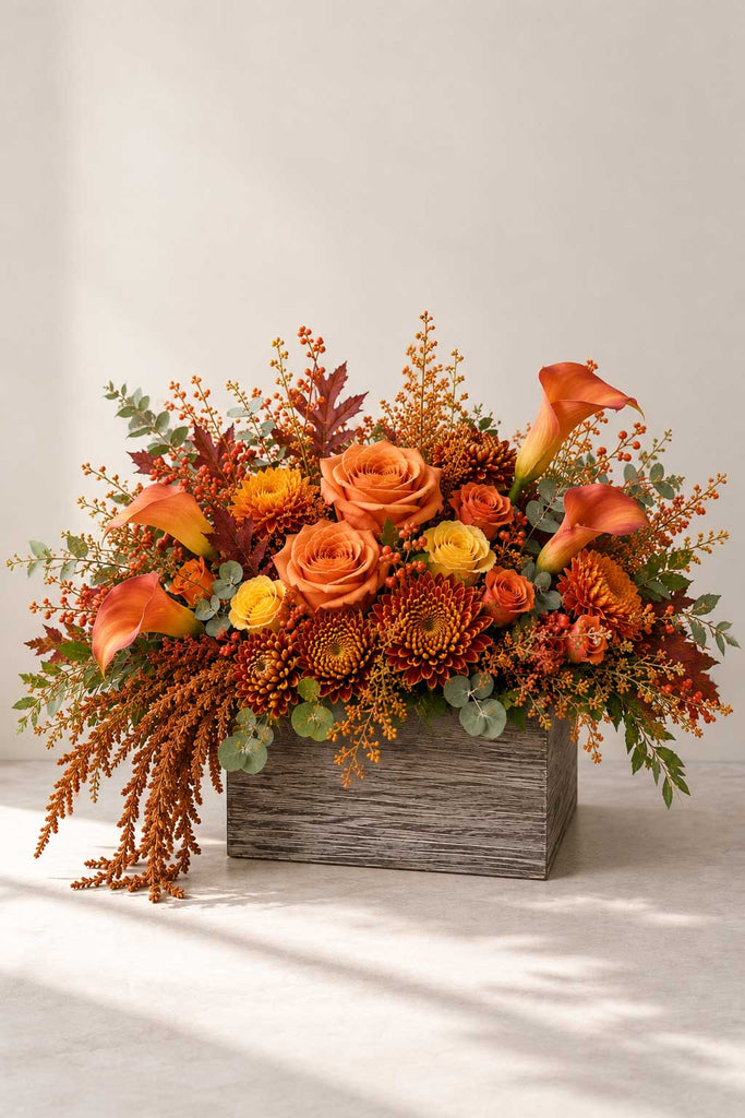 Canyon Glow fall floral arrangement with orange roses, calla lilies, chrysanthemums, eucalyptus, berries, and autumn foliage in a rustic wooden box.