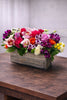 Cheerful floral arrangement in a rustic wooden box with roses, cymbidium orchids, colorful seasonal blooms, and fresh greenery.