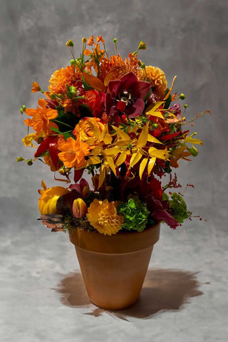 Topiary style fall arrangement with orange and yellow flowers and artificial fruits. 