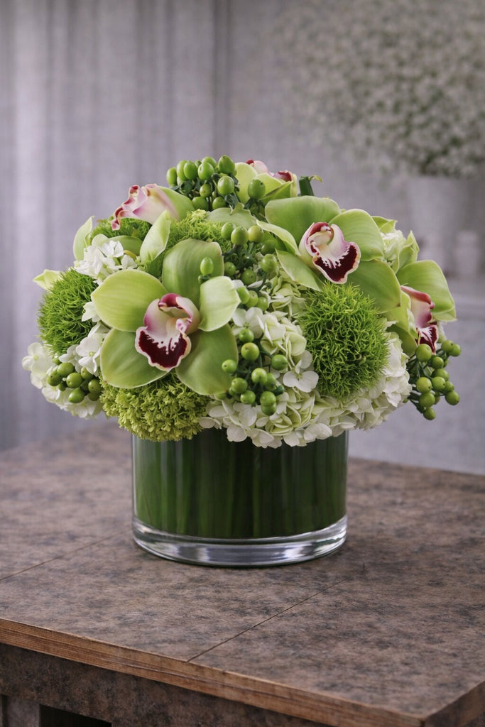 Fashionista Blooms floral arrangement in a clear glass cylinder vase with green cymbidium orchids, hydrangea, green textured blooms, and berry accents.