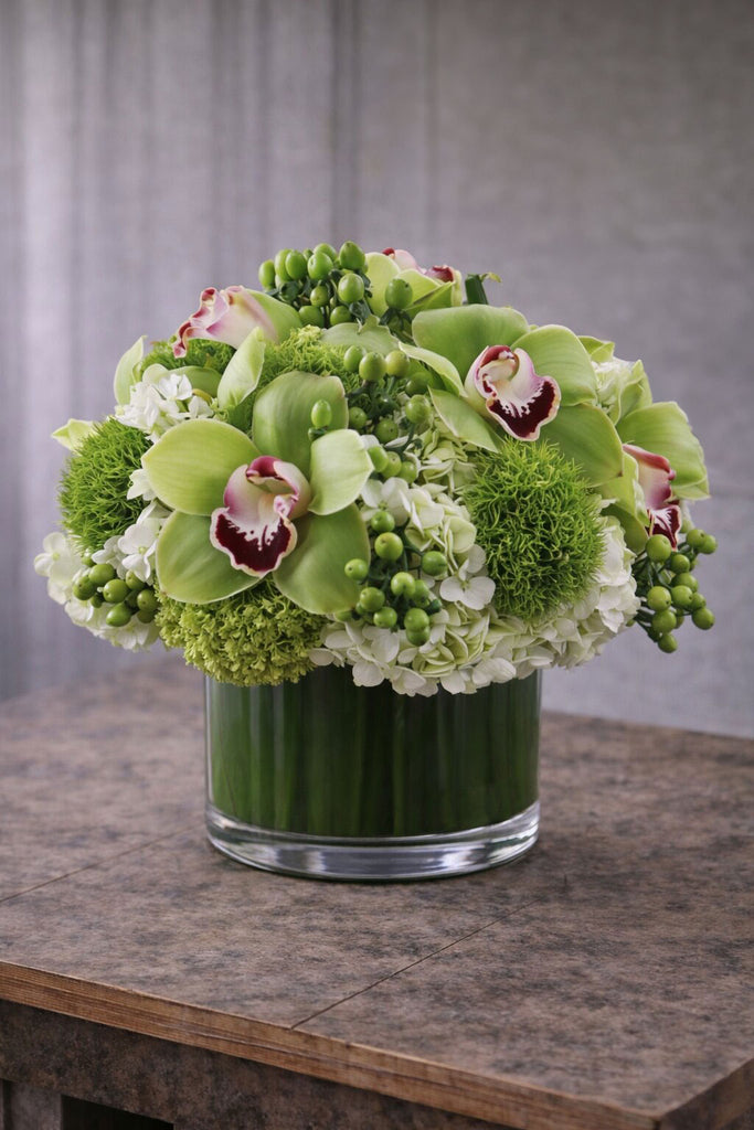 Fashionista Blooms floral arrangement in a clear glass cylinder vase with green cymbidium orchids, hydrangea, green textured blooms, and berry accents.