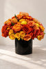 Golden Dawn floral arrangement with orange, amber, and yellow roses, pincushion blooms, and citrus accents in a black vase.