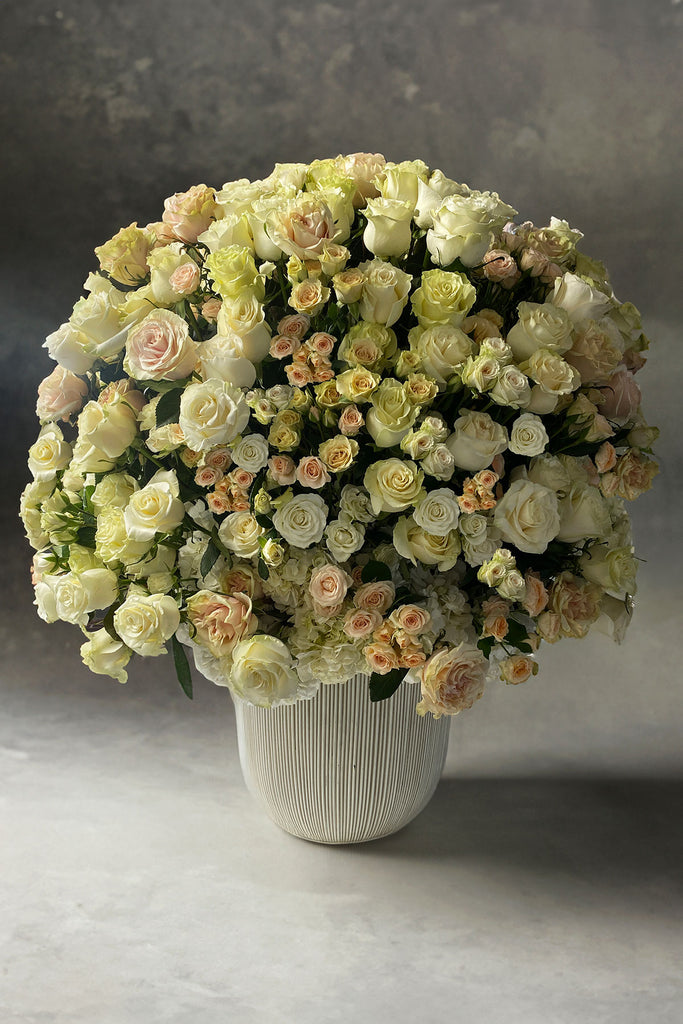 Extra large luxury floral arrangement with ivory, blush, and cream roses, spray roses, and hydrangea in a modern textured vase, designed in a lush dome shape.