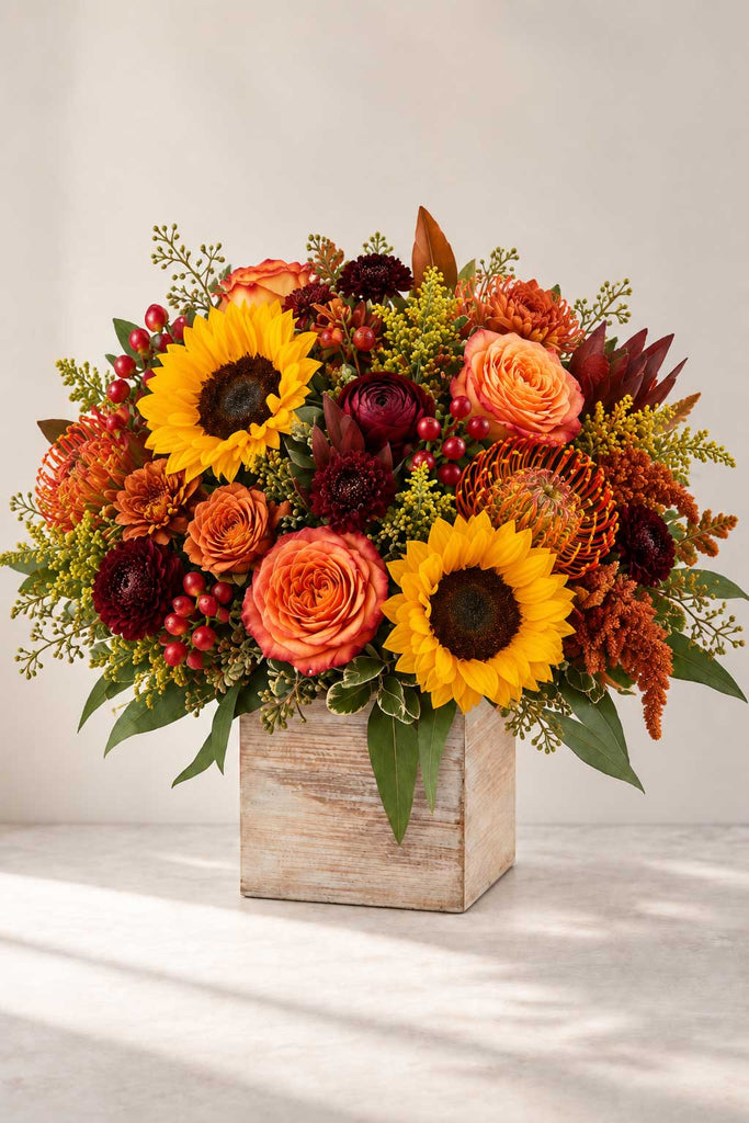 Hello Autumn floral arrangement with sunflowers, orange roses, pincushion protea, burgundy blooms, berries, and greenery in a rustic wooden box.