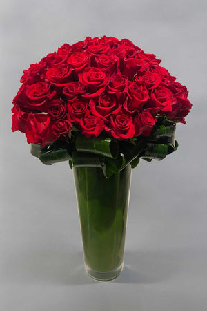 Red roses tightly arranged in a tall round vase
