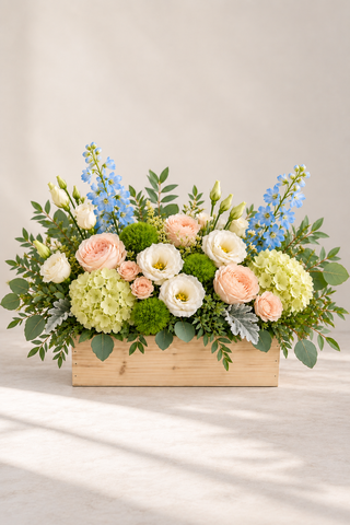 Meadow garden-style floral arrangement with blush roses, white lisianthus, green hydrangea, blue delphinium and greenery in a rectangular wooden box by Laguna Beach Florist