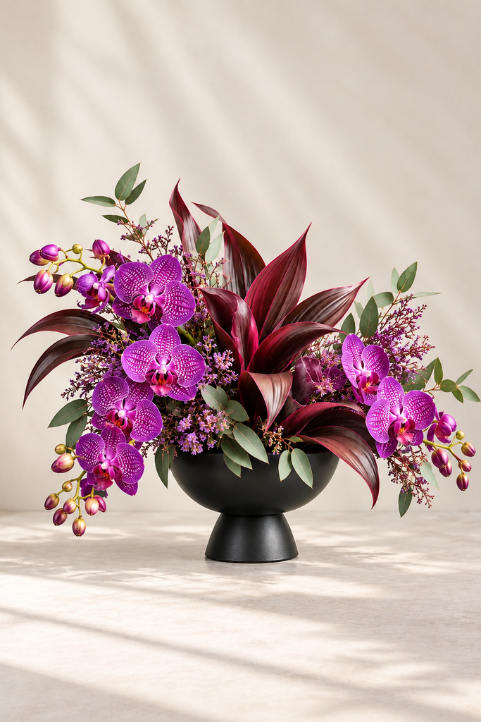 Merlot luxury purple orchid arrangement with burgundy foliage in a matte black pedestal bowl by Laguna Beach Florist