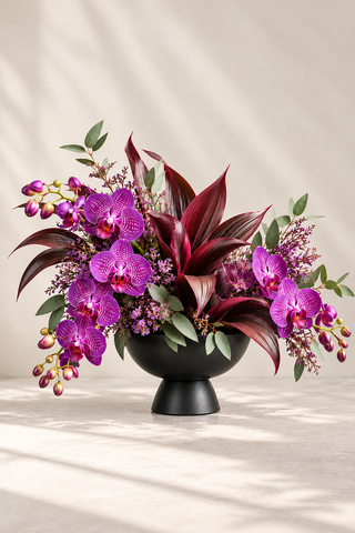 Merlot luxury purple orchid arrangement with burgundy foliage in a matte black pedestal bowl by Laguna Beach Florist