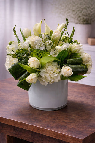 Minty Delight floral arrangement in a white glass vase with white calla lilies, hydrangea, tulips, roses, and fresh green accents.