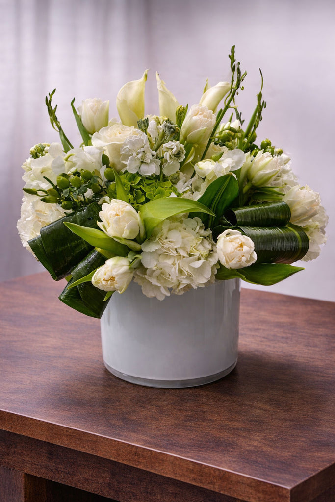 Minty Delight floral arrangement in a white glass vase with white calla lilies, hydrangea, tulips, roses, and fresh green accents.