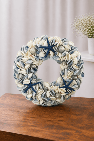 Dark blue Seashell wreath with starfish, pearls, and assorted natural shells displayed on a wooden table in a soft neutral setting.