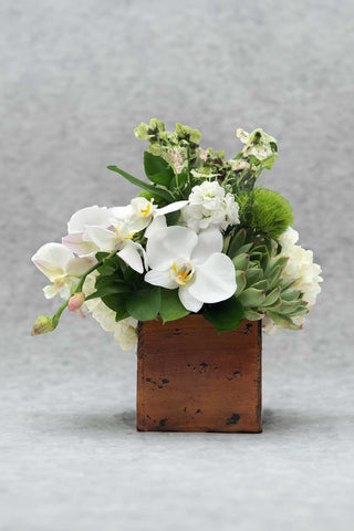 Floral arrangement with white flowers and greenery in a wooden box on a gray background