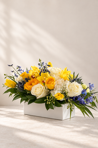 Posy yellow, white and blue all-around floral centerpiece in a white rectangular vase by Laguna Beach Florist
