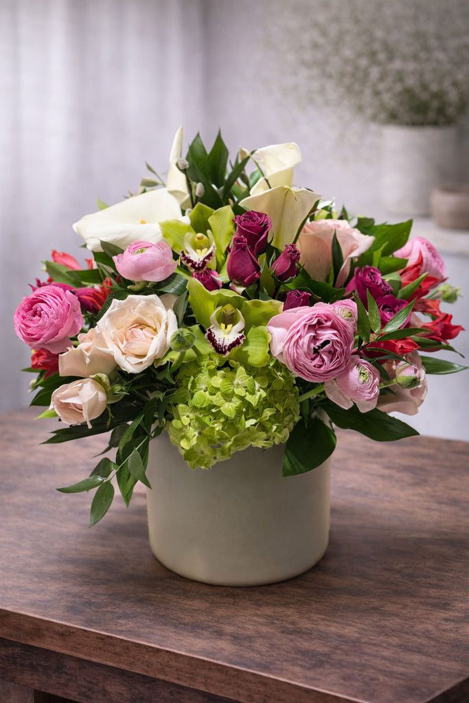 Radiant Bloom floral arrangement in a modern ceramic vase with roses, ranunculus, cymbidium orchids, hydrangea, calla lilies, and seasonal blooms.