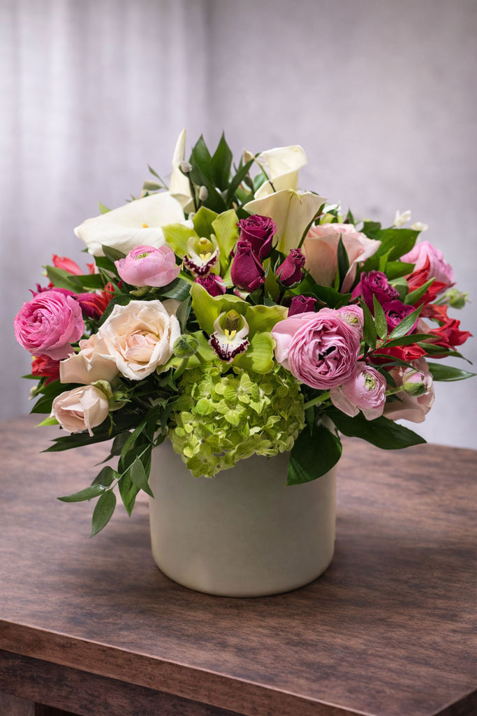 Radiant Bloom floral arrangement in a modern ceramic vase with roses, ranunculus, cymbidium orchids, hydrangea, calla lilies, and seasonal blooms.