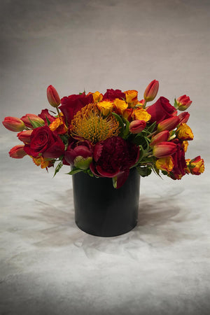Fall mixed flower arrangement with yellows and oranges in a black vase placed in front of gray background