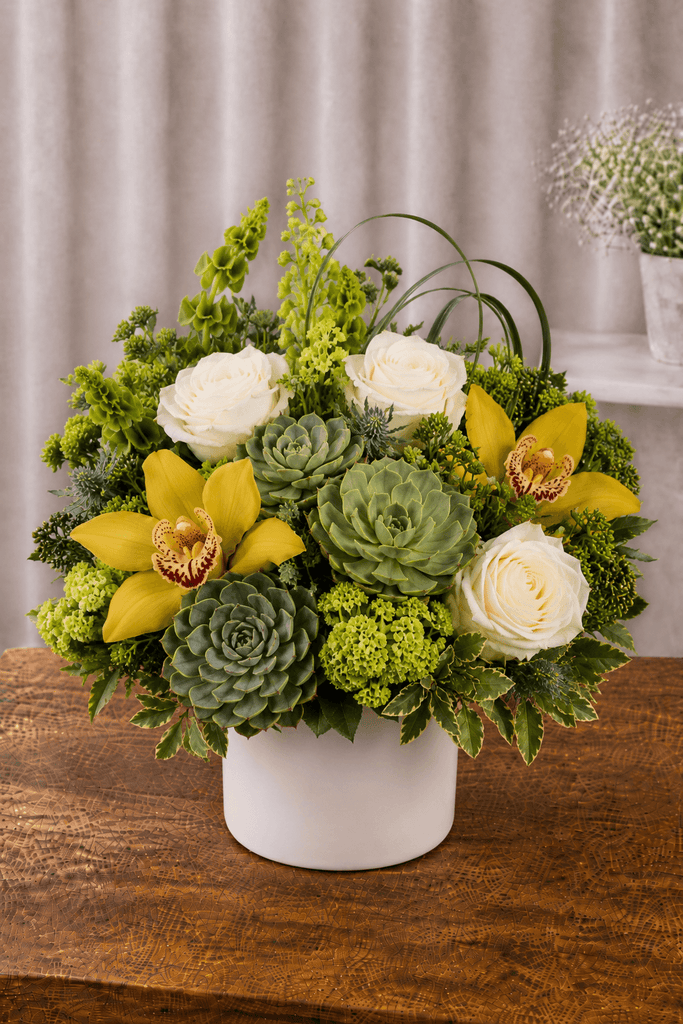 Alt Image Text:
White and yellow floral arrangement with white roses, yellow orchids, green accents, textured botanicals, and foliage in a white ceramic vase.