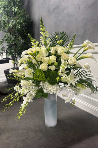 Tall luxury white flower arrangement with orchids, roses, lilies, and calla lilies in a frosted glass vase, approximately 45 inches tall.