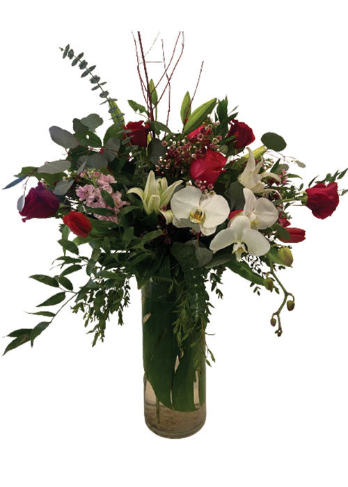 Mixed spring arrangement with colorful flowers arranged in a clear vase on a white background